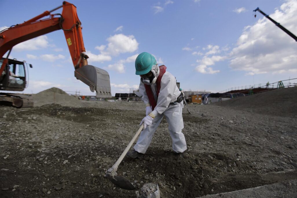עובד מנקה אדמה עם פסולת רדיואקטיבית בתחנה הגרעינית בפוקושימה. (צילום: Toru Hanai/Pool Photo via AP)