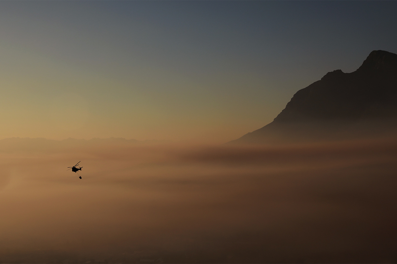 מסוק מרחף מעל העשן בעיר קייפטאון דרום אפריקה, 20 באפריל 2021. שריפת ענק המתפשטת במורדות הר השולחן המפורסם נשארה תחת שליטה.כבאים ומסוקים ניצלו את הרוחות הנמוכות כדי להכיל את השריפה. (AP Photo/Nardus Engelbrecht)