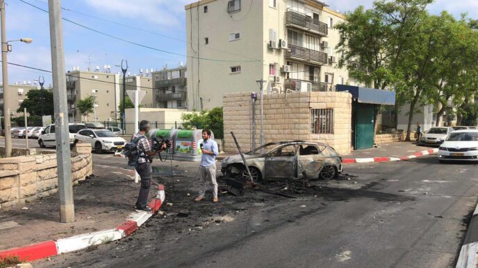 A reporter speaking about the Akko riots in front of a burned car. (Photo: Omer Cohen)