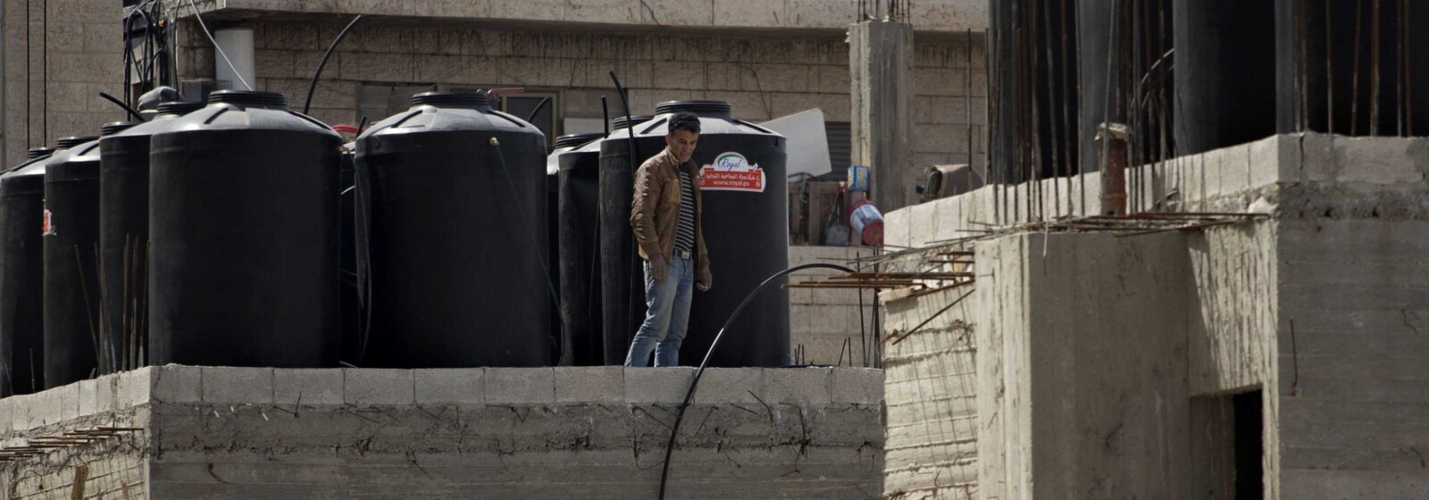 פועל ממזרח ירושלים לצד מיכלי מים על גג בשועפאט. "יש כאן משהו שבסוף יתפוצץ" (צילום: AP Photo/Sebastian Scheiner)