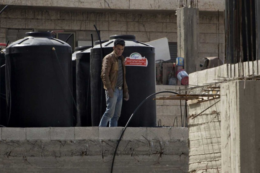 عامل من شرقي القدس إلى جانب صهاريج مياه على سطح بيت في شعفاط. "يوجد هنا شيء الذي في النهاية سينفجر" (تصوير: AP Photo / Sebastian Scheiner)