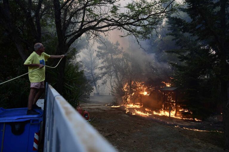 אזרח יווני משפריץ מים על עצים שעלו באש בזמן שריפת ענק באזור אדאדמס, צפונית לאתונה. מאות בני אדם שמתגוררים באזור היער צפונית לבירה נמלטו מבתיהם בגלל הלהבות. (צילום:AP Photo/Michael Varaklas)