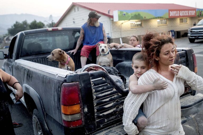 דסטיני ברנרד מחזיקה את ריימונד ויליאם גצ'יוס בזמן שהם נצורים בתחנת דלק ליד 'שריפת דיקסי'. ברנרד עזרה לגצ'יוס ובני משפחתו להתפנות מביתם בעיירה סוזנוויל כשמכוניתה התקלקלה. (צילום: AP Photo/Noah Berger)