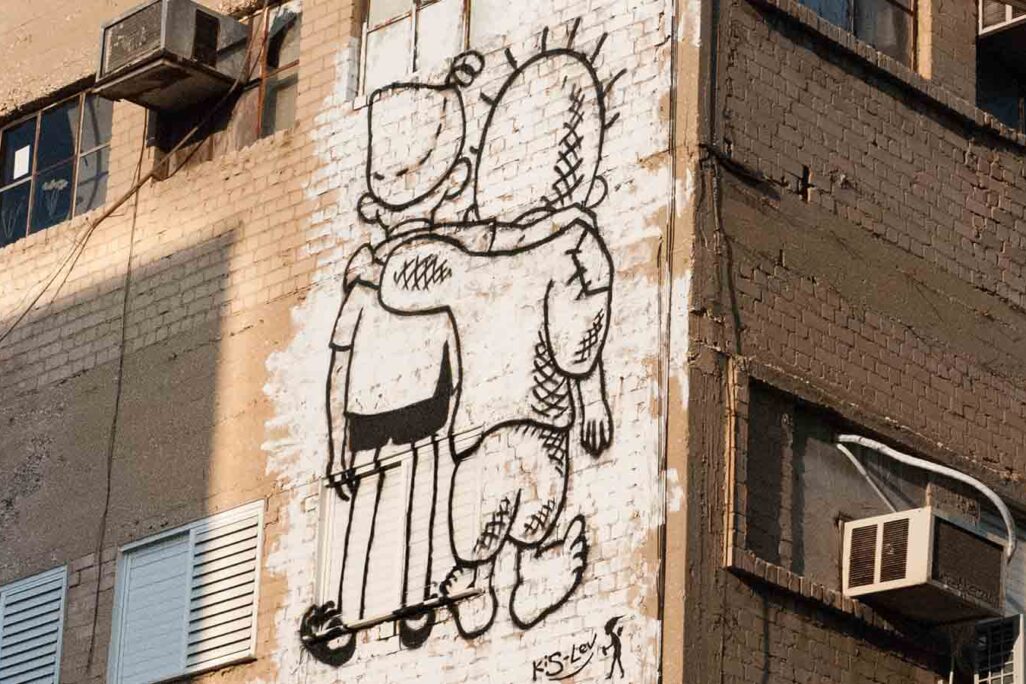 The Handalah character by the Egyptian artist Naji El Ali and the Srulik character by the Israeli cartoonist Dosh hold each other, in street art by Yonatan Kis-Lev (Photo: Psychology Forever / Wikimedia)