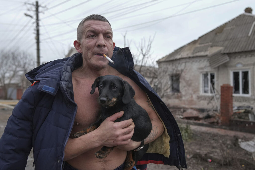 A man holds a dog as he walks past a damaged house following Russian shelling, in Mariupol, Ukraine, Thursday, Feb. 24, 2022. (Photo: AP Photo/Evgeniy Maloletka)