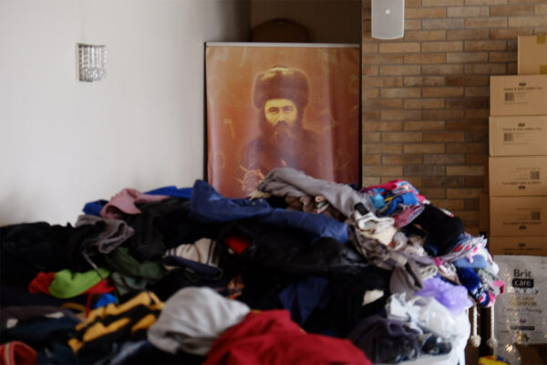 ערימת בגדים שנתרמו עבור הפליטים. בתמונה על הקיר: רבי מאיר שפירא מייסד ישיבת לובלין (צילום: דוד טברסקי)