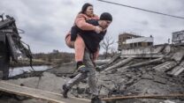 גבר נושא אישה כשהם חוצים שביל מאולתר בזמן שהם בורחים מהעיר אירפין (צילום: AP Photo/Oleksandr Ratushniak)