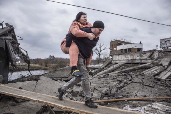 גבר נושא אישה כשהם חוצים שביל מאולתר בזמן שהם בורחים מהעיר אירפין (צילום: AP Photo/Oleksandr Ratushniak)