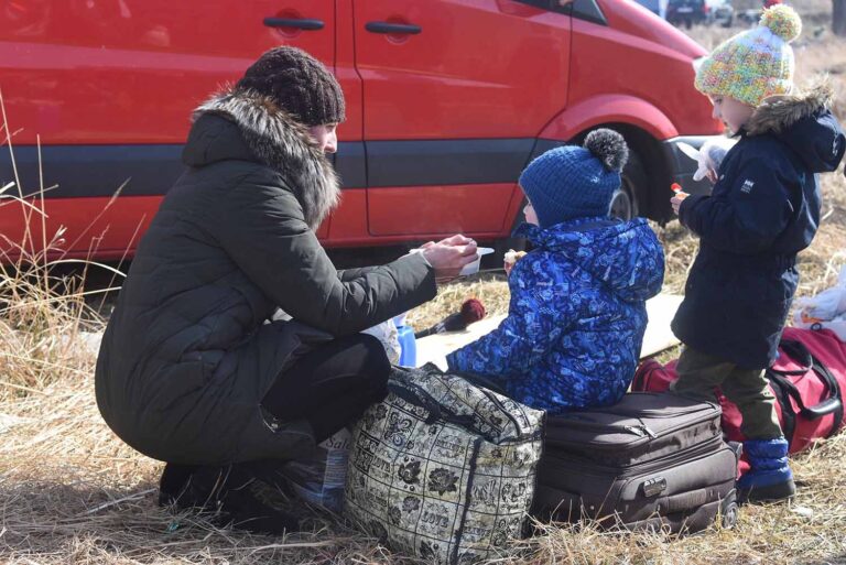 ילדים בשדה על מזוודות, אוכלים מרק חם שמתנדבת מגישה להם (צילום: דן לזר)
