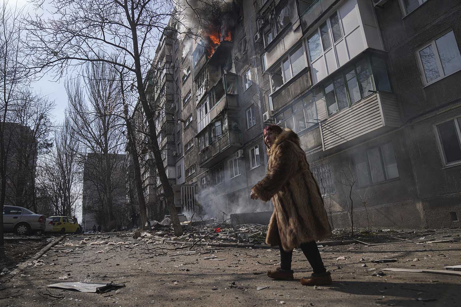 אישה חולפת על פני בניין דירות בוער לאחר הפגזות במריופול (צילום: AP Photo/Evgeniy Maloletka)