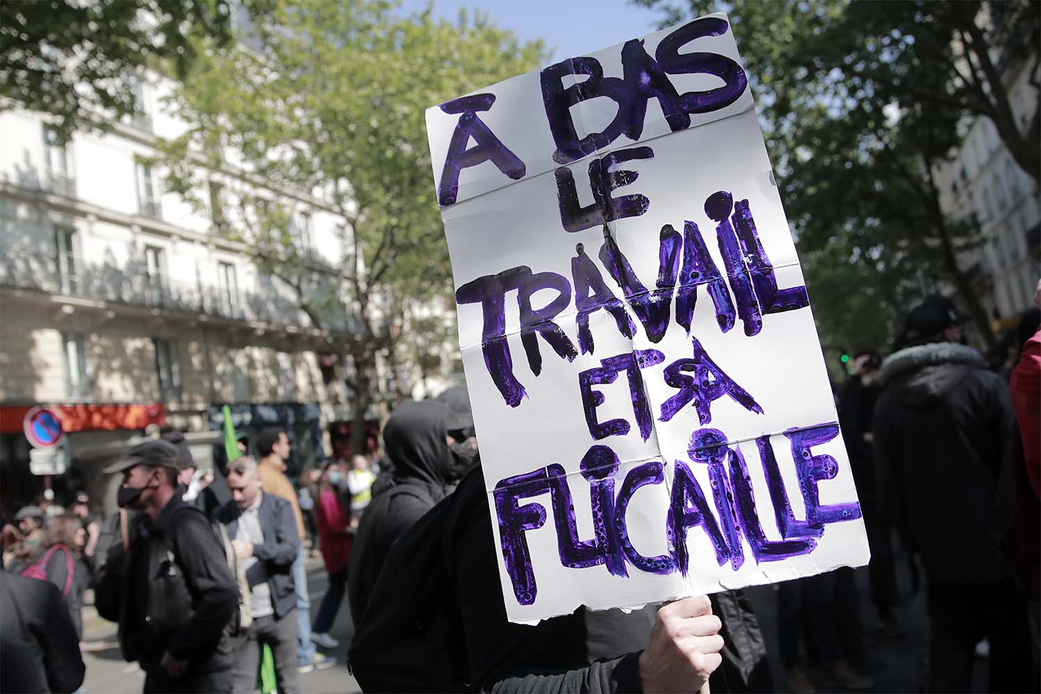 המפגינים אוחזים בכרזה שבה נכתב: &quot;הפסקת העבודה והשוטרים שלה&quot; במהלך הפגנה באחד במאי בפריז. (צילום: AP Photo/Lewis Joly)
