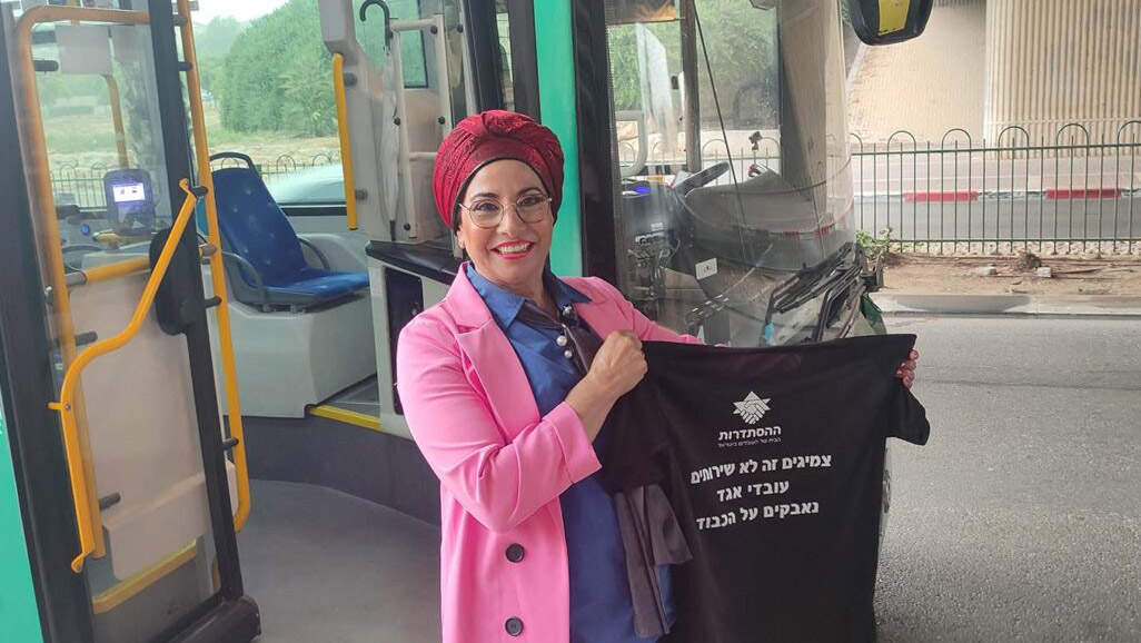 Bus driver Sigalit Mergui holds up a protest shirt. “Men can use the bathroom on the street, which is unpleasant and inappropriate. But what is a religious woman meant to do?” (Photo: Nizzan Zvi Cohen)