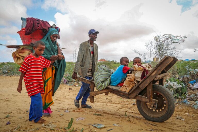 תושב מוגדישו עוזר לאישה שמגיעה למחנה העקורים עם ילדיה. 7 מיליון מתוך 16 מיליון תושבים צפויים לסבול ממחסור במזון (צילום: AP Photo/Farah Abdi Warsameh)
