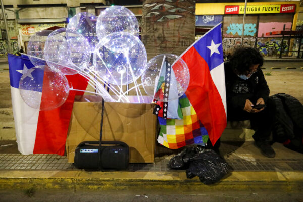 מוכר מזכרות לתמיכה בחוקה החדשה של צ'ילה יושב ומקשיב לחדשות בנושא משאל העם (צילום: AP Photo/Cristobal Escobar)