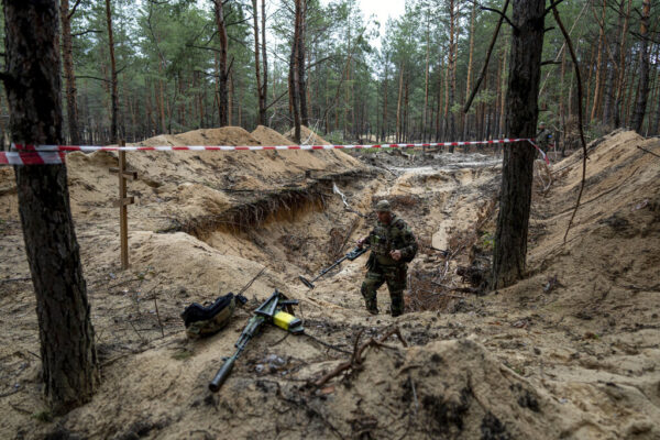 חייל אוקראיני בודק באמצעות גלאי מתכות היתכנות של הימצאות חומרי נפץ באחד הקברים (צילום: AP Photo/Evgeniy Maloletka)