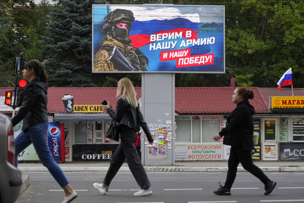 אנשים בלוהסנק שבמזרח אוקראינה, חולפים על פני שלט חוצות המציג חייל ודגל רוסי, וקורא "אנחנו מאמינים בצבא שלנו ובניצחון שלנו" (צילום: AP)