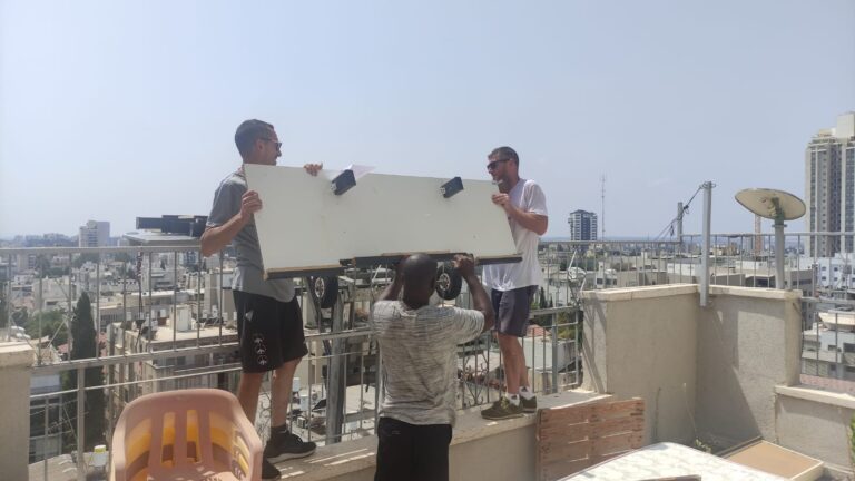 אלישה, ישראל ותומאש בקומה 8 בבניין ברחובות, נעזרים במנוף כדי להעביר את הציוד (צילום: ניצן צבי כהן)