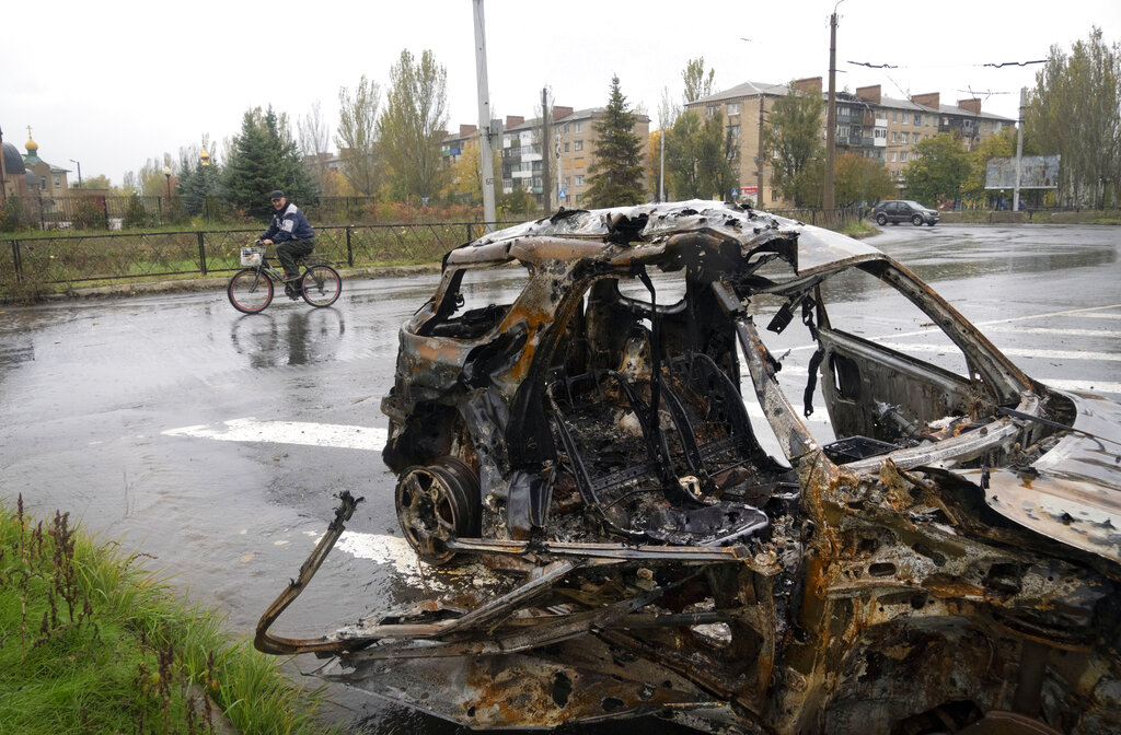 אדם רוכב על אופניים ליד רכב שנהרס מהפצצות כוחות רוסים במרכז העיר בחמוט שבמחוז דונצק במזרח אוקראינה, 26 באוקטובר 2022 (AP Photo/Efrem Lukatsky)