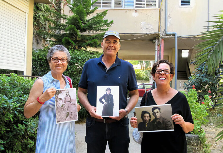 תמי והאחים דודו ואורנה עם תמונות הוריהם במדים ברקע הבית שבו גדלו (צילום: יעל הורוביץ)