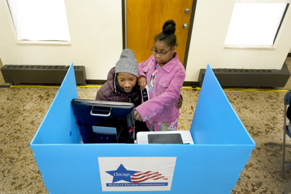 כריסטופר סנדריג' מצביע בבחירות האמצע בארה"ב בקלפי בשיקגו, ומלמד את בתו כריסטינה על תהליך ההצבעה (AP Photo/Charles Rex Arbogast)