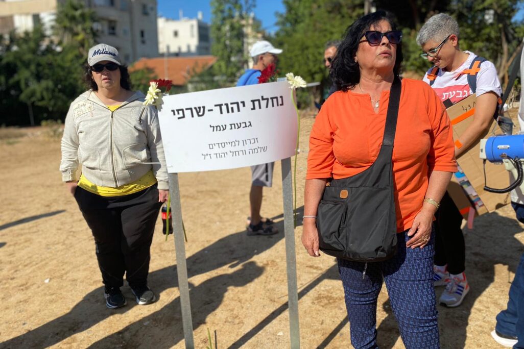ציונה יהוד (בחולצה הכתומה)  ליד שלט שמציין היכן הייתה הנחלה המשפחתית שלה: "אם הייתי צעירה הייתי עוזבת את הארץ" (צילום: יהל פרג')