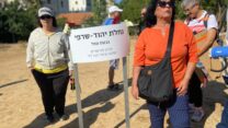 ציונה יהוד (בחולצה הכתומה)  ליד שלט שמציין היכן הייתה הנחלה המשפחתית שלה: "אם הייתי צעירה הייתי עוזבת את הארץ" (צילום: יהל פרג')