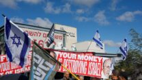 A protest in front of the Forum Kohelet offices in Jerusalem, with a sign showing pictures of Jeffrey Yass and Arthur Danchik, the American billionaires who donate to the forum, with the caption "Your money is destroying Israel." (Photo: Reuters/Ammar Awad)