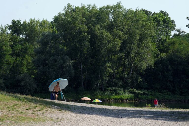 אדם נושא שמשיית חוף בזמן שהאנשים מתקררים על גדות נהר טיצ'ינו בגשר הסירות ליד מילאנו, איטליה. גל חום עז הגיע לאיטליה, מביא איתו טמפרטורות קרובות ל-40 מעלות (צילום AP/אנטוניו קלאני)