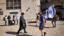 A demonstrator heading to the Knesset to protest the judicial reforms crosses paths with someone on his way back from morning prayers. (Photo: Haim Goldberg/Flash 90)