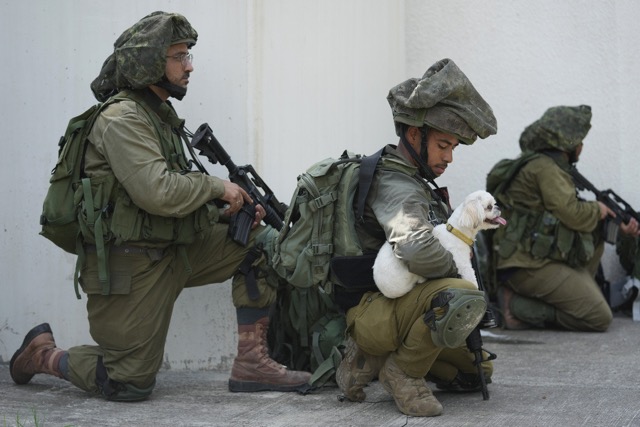 An Israeli soldier holds a dog in kibbutz Kfar Azza on Tuesday, Oct. 10, 2023. Hamas militants overran Kfar Azza on Saturday, where many Israelis were killed and taken captive. (AP Photo/Erik Marmor)