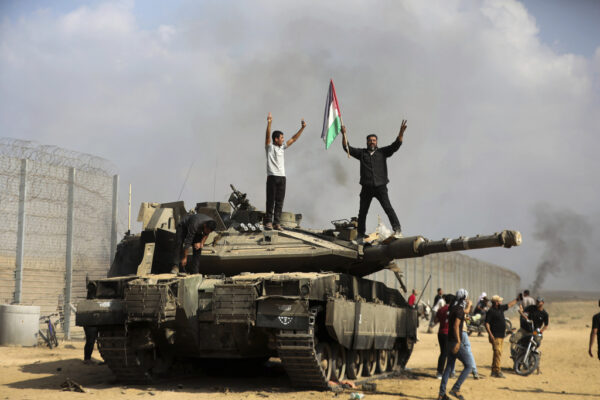 פלסטינים מרצועת עזה חוגגים ומניפים דגלי פלסטין על טנק ישראלי הרוס סמוך לגדר הגבול, מזרחית לחאן יונס, ב-7 באוקטובר (צילום: AP Photo/Yousef Masoud)