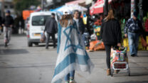 אישה עטופה בדגל ישראל בשוק הכרמל בתל אביב (צילום אילוסטרציה: מרים אלסטר / פלאש 90)