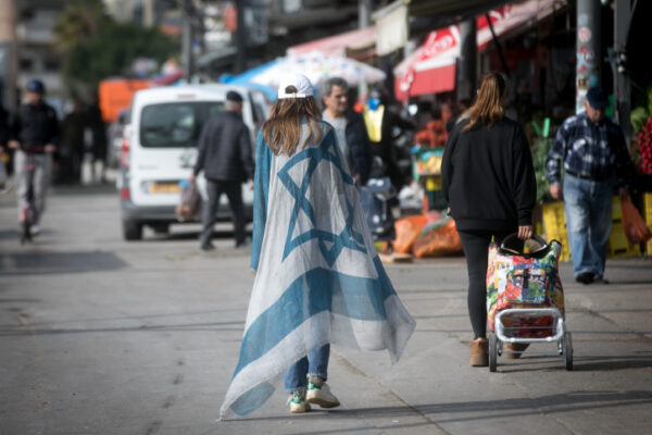 אישה עטופה בדגל ישראל בשוק הכרמל בתל אביב (צילום אילוסטרציה: מרים אלסטר / פלאש 90)
