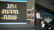 אישה עם עגלה חולפת על פני שלט של עיריית תל אביב לתמיכה במשפחות החטופים לקראת חג הפסח (צילום: מרים אלסטר/פלאש90)