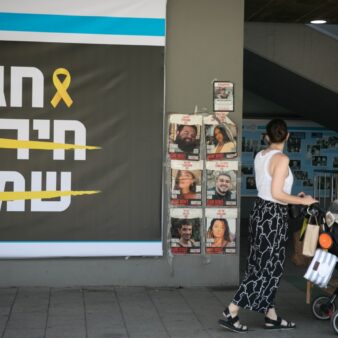 אישה עם עגלה חולפת על פני שלט של עיריית תל אביב לתמיכה במשפחות החטופים לקראת חג הפסח (צילום: מרים אלסטר/פלאש90)