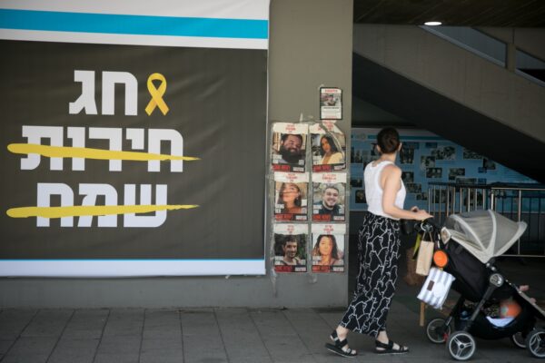 אישה עם עגלה חולפת על פני שלט של עיריית תל אביב לתמיכה במשפחות החטופים לקראת חג הפסח (צילום: מרים אלסטר/פלאש90)