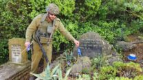 אחד מלוחמי כיתת הכוננות במשגב עם מניח דגל על קברו של חלל בבית העלמין בקיבוץ המפונה (צילום: דוברות הקיבוץ)