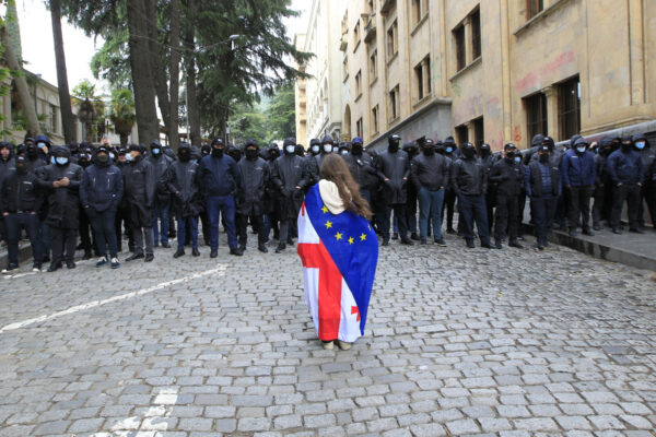 מפגינה עטופה בדגל גאורגיה והאיחוד האירופי מול כוחלות משטרה גדולים סמוך לפרלמנט הגאורגי, לקראת ההצבעה על "חוק הסוכנים הזרים" (צילום: AP Photo/Shakh Aivazov)