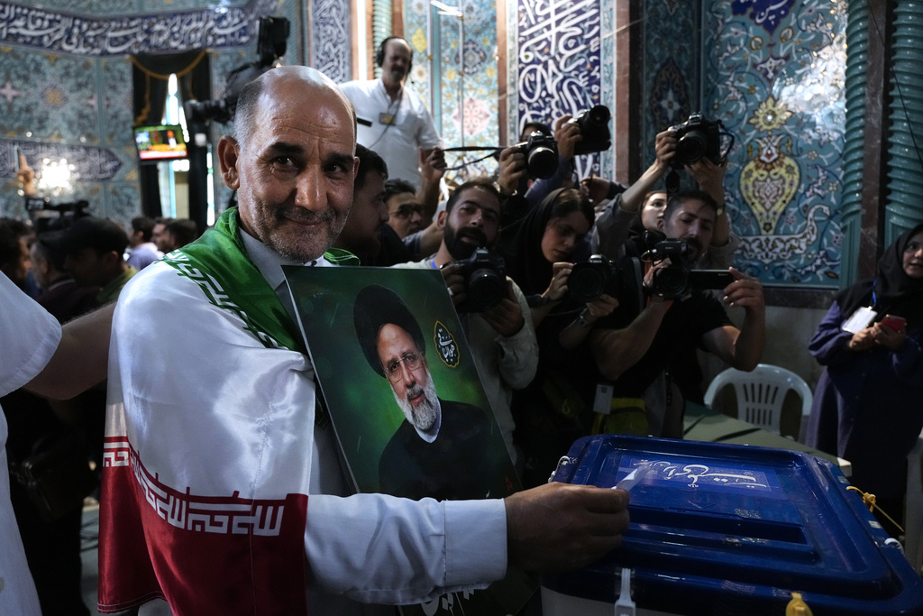 אזרח איראני מצביע בקלפי בטהראן בבחירות לנשיאות איראן, ואוחז את תמונתו של הנשיא הקודם איבראהים ראיסי, שנהרג בהתרסקות מסוק (AP Photo/Vahid Salemi)