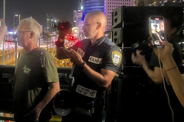 שוטר מצלם בווידאו את משפחות החטופים שבהפגנה בגשר בגין (צילום: אורן דגן)