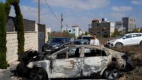 פלסטינים סמוך לרכב שנהרס בהתפרעויות של עשרות יהודים בכפר ג'ית שבשומרון (AP Photo/Nasser Nasser)