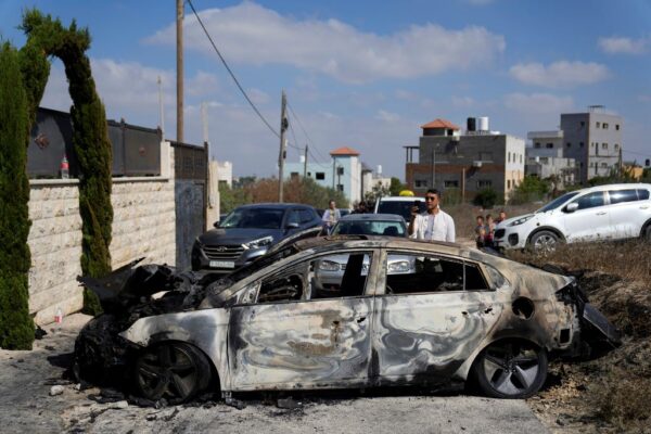 פלסטינים סמוך לרכב שנהרס בהתפרעויות של עשרות יהודים בכפר ג'ית שבשומרון (AP Photo/Nasser Nasser)