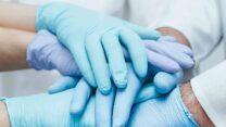 Team of medical workers in blue gloves holding hands together. Closeup. Unity concept.