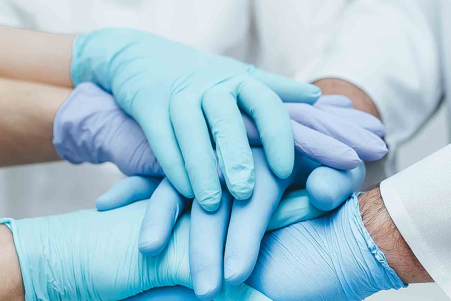 Team of medical workers in blue gloves holding hands together. Closeup. Unity concept.