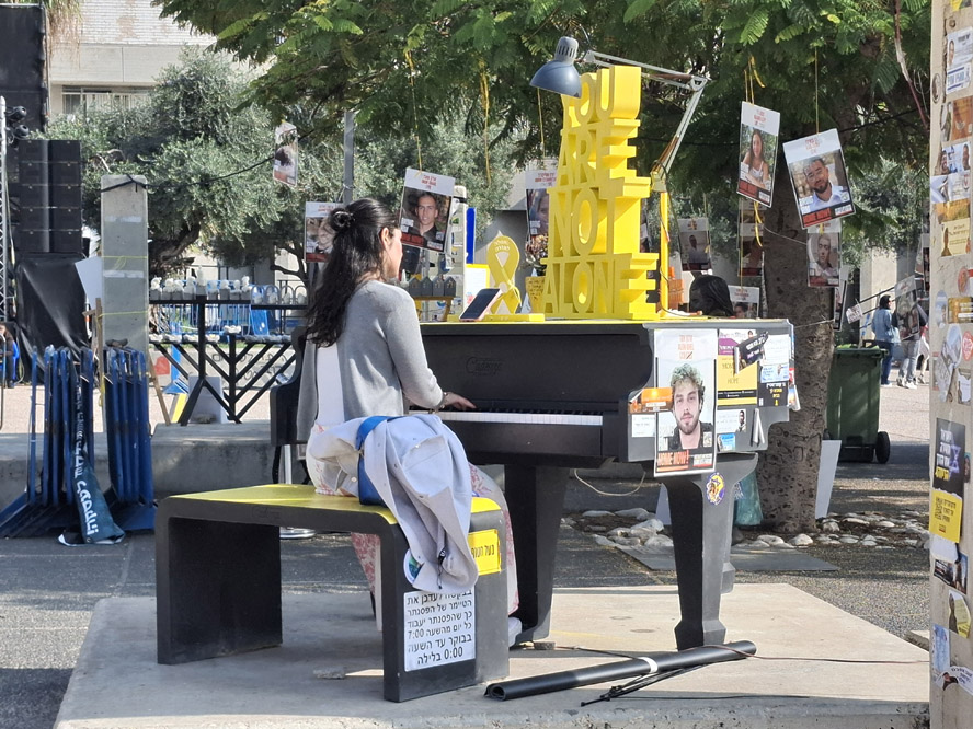 אישה מנגנת על הפסנתר שהוצב בכיכר החטופים בקריאה להשבת החטוף אלון אהל (צילום: הדס יום טוב)