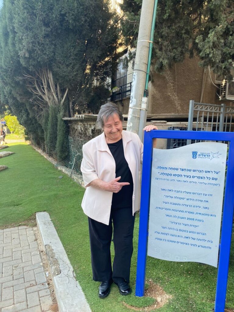 ליד הברוש ברחוב עצמאות 51 בהרצליה, עם שלט שמספר על השיר "מקהלה עליזה" (צילום: אלבום פרטי)