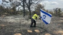 נהג כבאית בקק״ל רן נעים, מניף את דגל ישראל בלב השריפה בפארק קנדה (צילום: קק"ל)