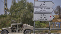 רכבים צה"ליים ליד קיבוץ נחל עוז, לצד שלט שהוצב במקום הקורא לשחרור החטוף עמרי מירן (צילום: AP Photo/Ohad Zwigenberg)