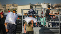 פלסטינים עם שקי מזון מחוץ לנקודת החלוקה של הקרן ההומניטרית לעזה (GHF) בדיר אל-בלח (צילום ארכיון: עלי חסן / פלאש 90)