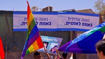 דגלי גאווה במצעד, כשברקע שלטים שנתלו ברחוב נגד הקהילה הלהט"בית (צילום: ארז וולך)